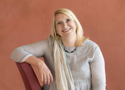 Portraitfoto: Kerstin Rosenberg sitzt seitlich auf einem Stuhl und schaut in die Kamera.